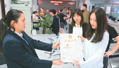 河北省承德市網絡代購經營者陳晨(右)從工作人員手中接過帶有統(tǒng)一社會信用代碼的營業(yè)執(zhí)照。 劉環(huán)宇攝(人民圖片)